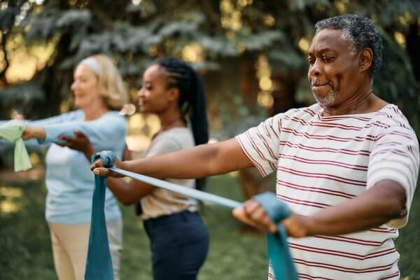 Older African American using stretch bands during a workout class to keep in shape as he ages.