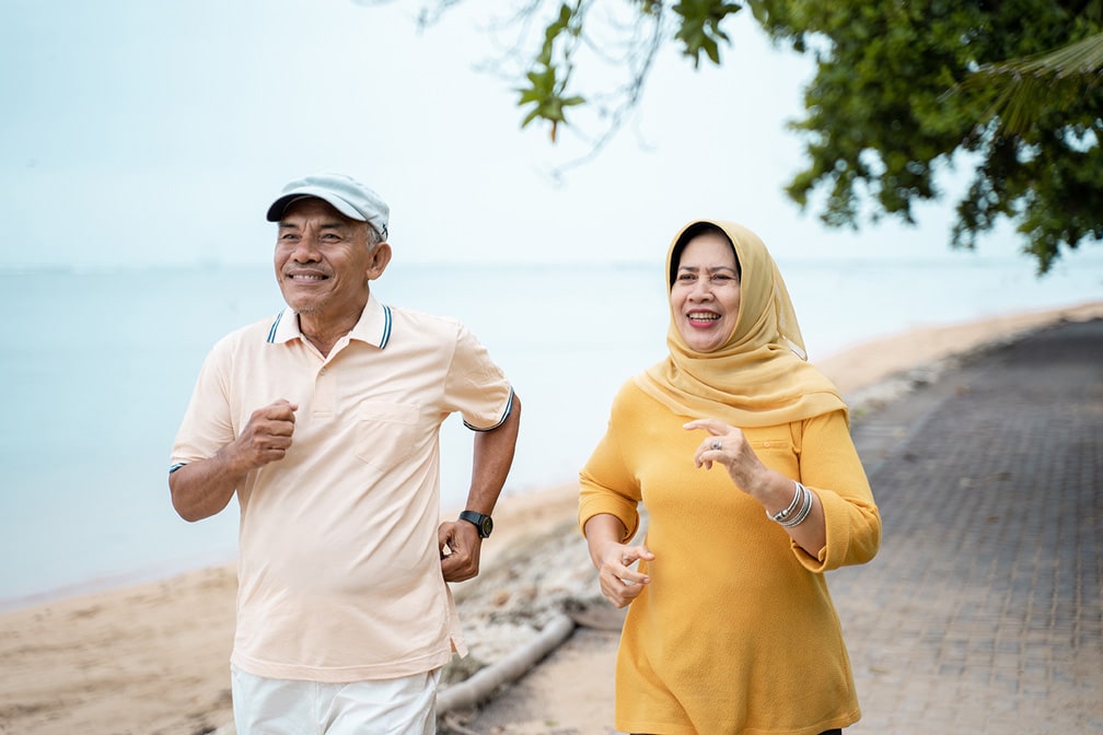 An older Arabic couple jogging alongside a beach on a cool day