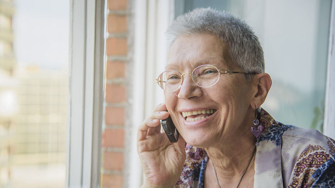 Older adult on the phone, smiling as she chats with someone from the Senior Alliance and the Friendly Reassurance program.