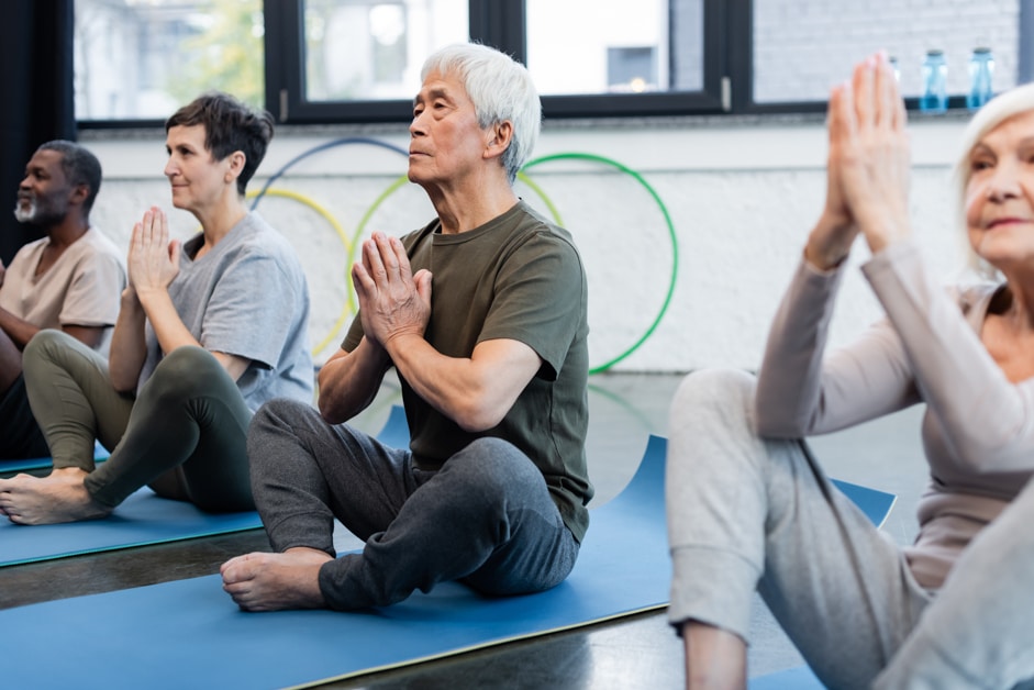mixed group of older adults doing exercise class which features yoga for balance