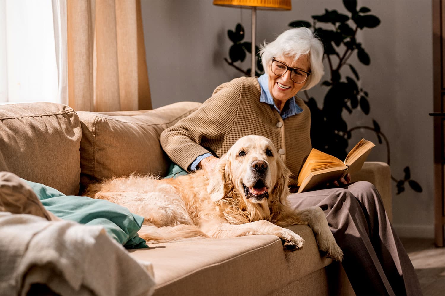 Older adult at home reading a book with her dog