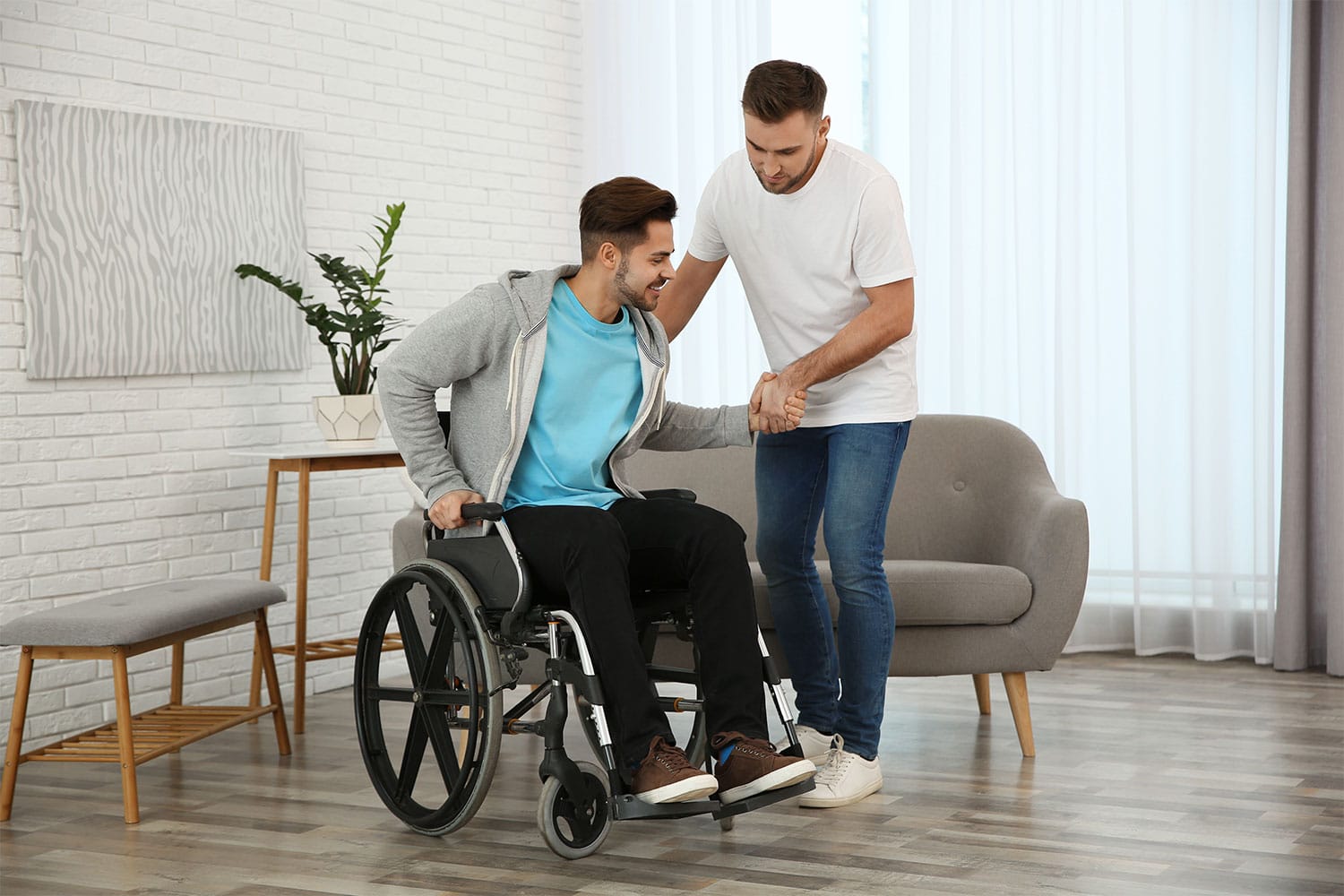 middle-aged adult with living with a disability receives help from a caregiver as he transitions from his wheelchair to a couch