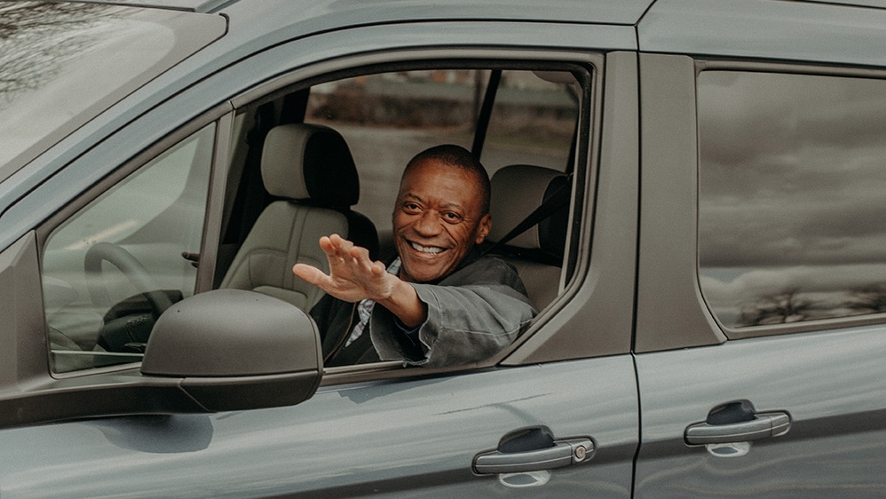 At The Senior Alliance in the Transportation program an African American driver sits in a green van with a smile to wave at a participant