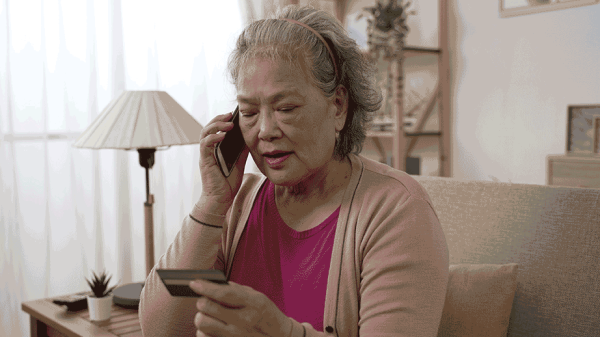 older adult chatting on the phone while looking at her credit card because someone is trying to scam her into giving her card number