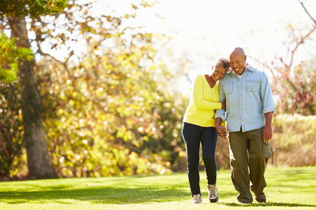 An older couple walking in the fall with green grass and vibrant trees