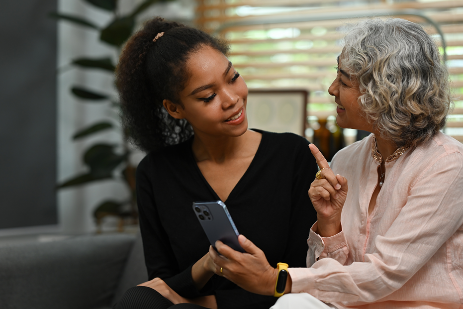 A grandmother and daughter sitting side by side on the couch, and the grandmother is holding a phone.