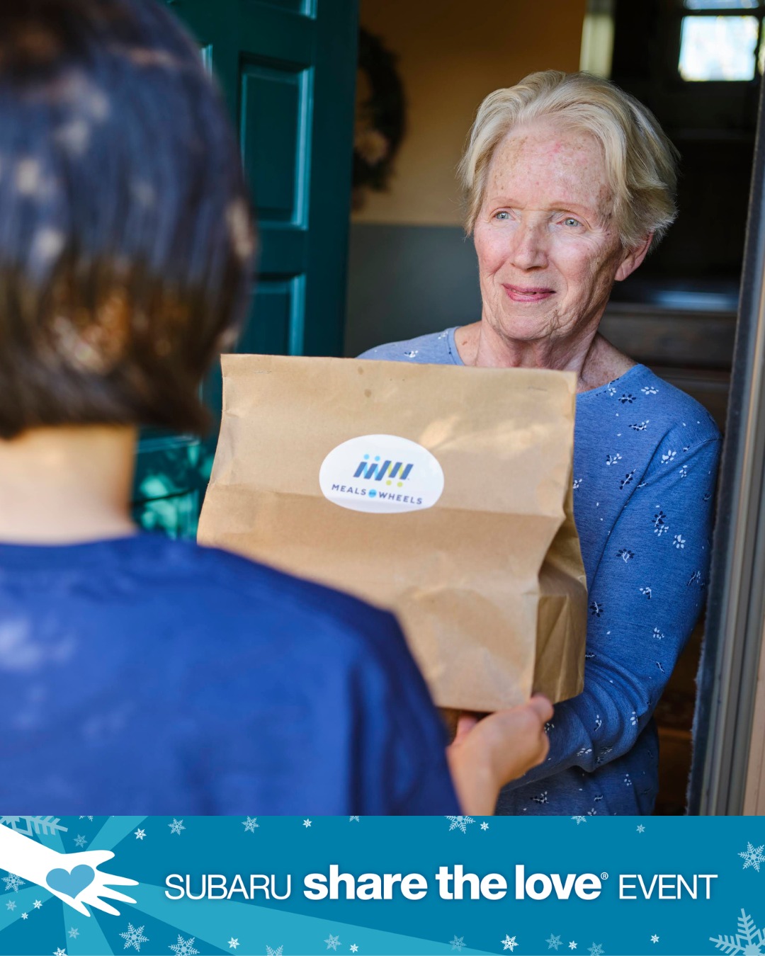 From Subaru's Share the Love Event supporting Meals on Wheels. An older home owner accepts a home-delivered meal from a young volunteer.