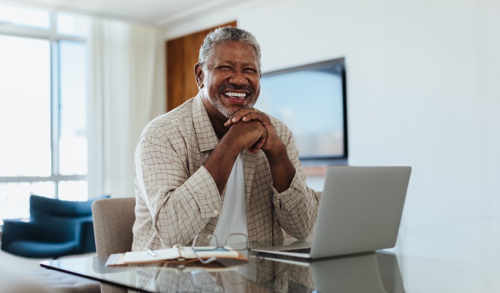 Cheerful senior man writing a letter to his legislator from his laptop.