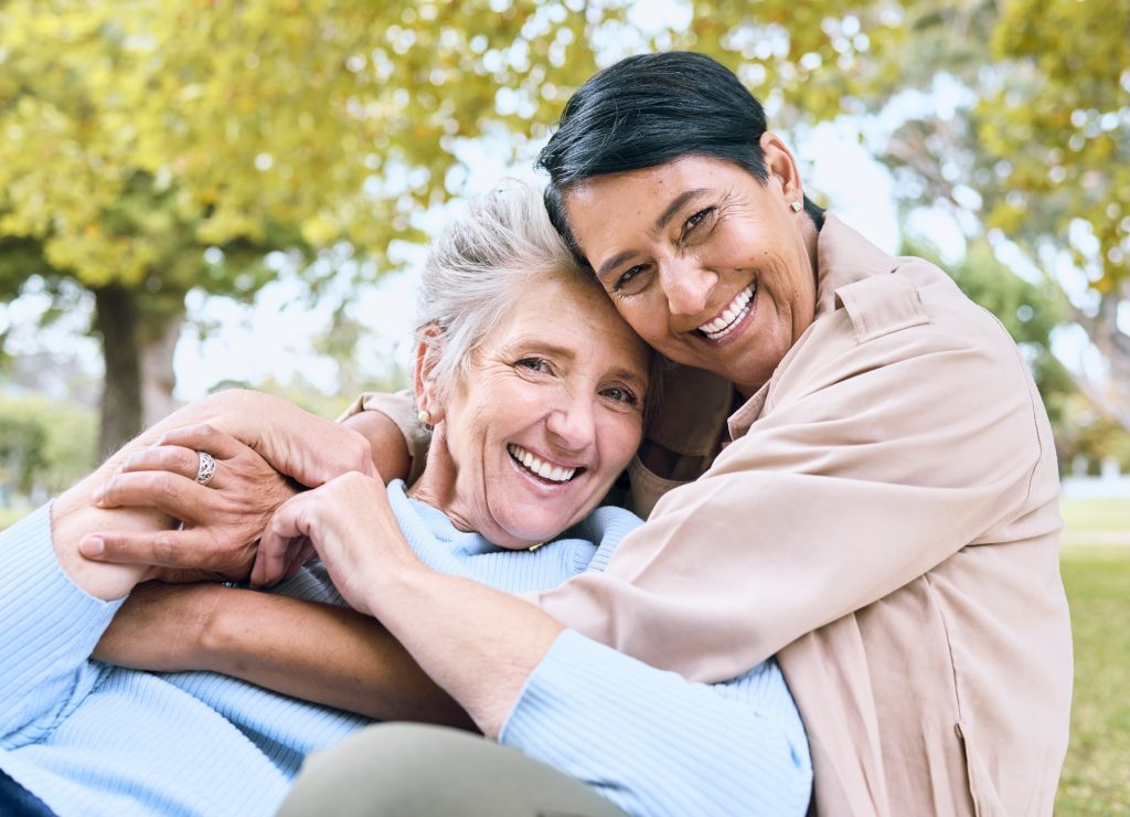 Happy elderly LGBTQ+ women in bonding embrace in community backyard.