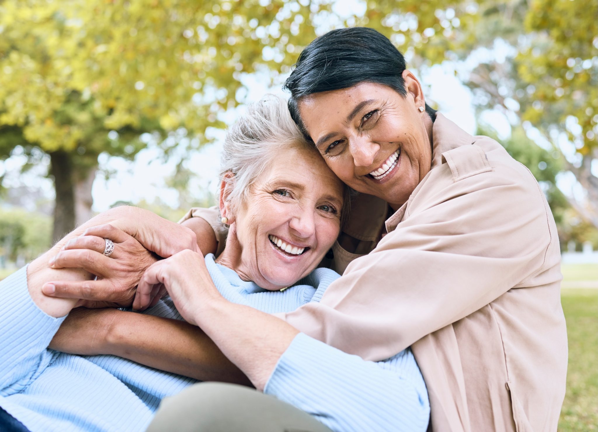 Happy elderly LGBTQ+ women in bonding embrace in community backyard.