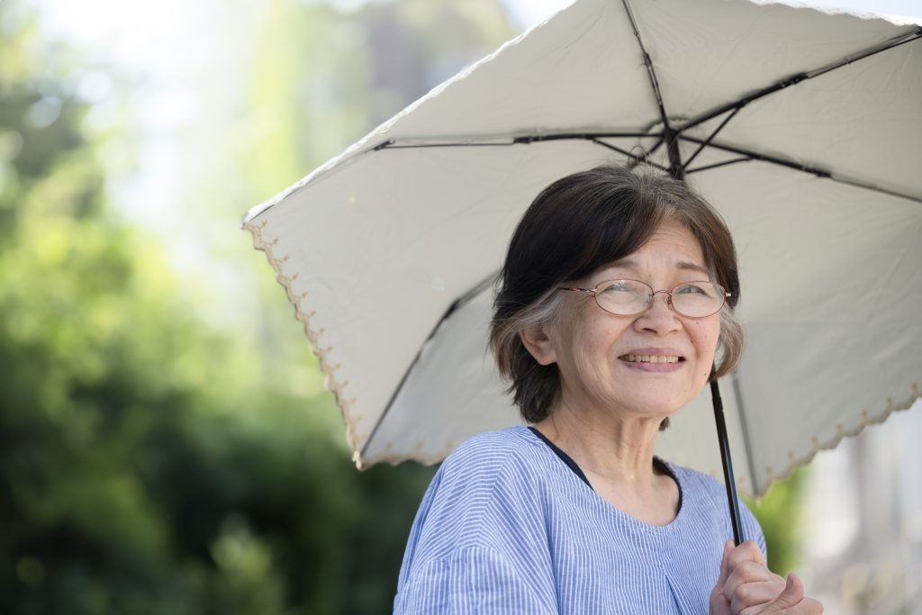 An older woman uses a parasol on a summer day to avoid heat exhaustion.