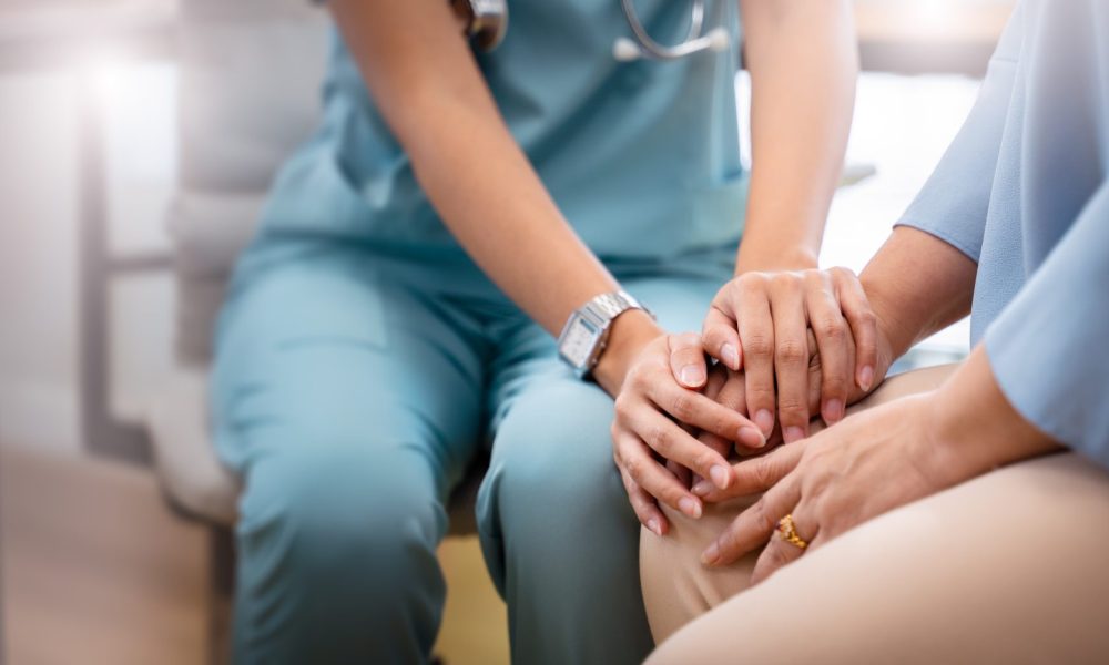 Doctor and elderly patient discuss hospice care options. Close up of their hands clasped together is the primary feature.