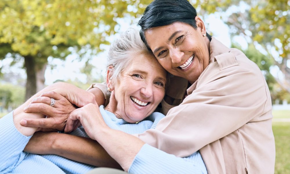 Happy elderly LGBTQ+ women in bonding embrace in community backyard.