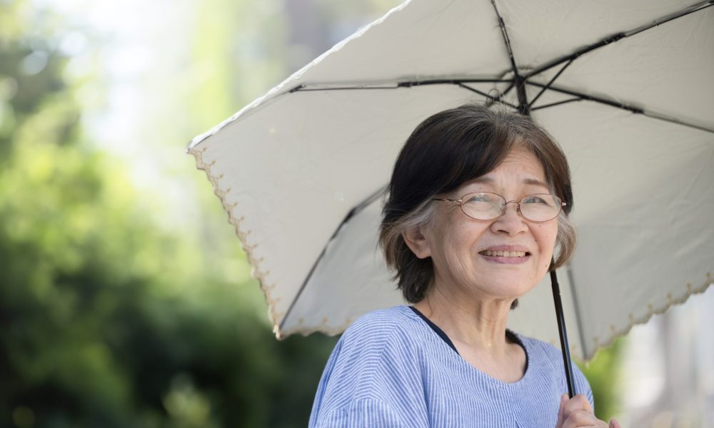 An older woman uses a parasol on a summer day to avoid heat exhaustion.