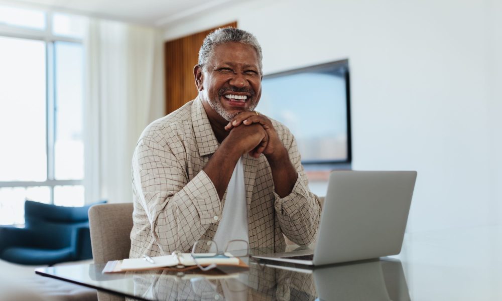 Cheerful senior man writing a letter to his legislator from his laptop.
